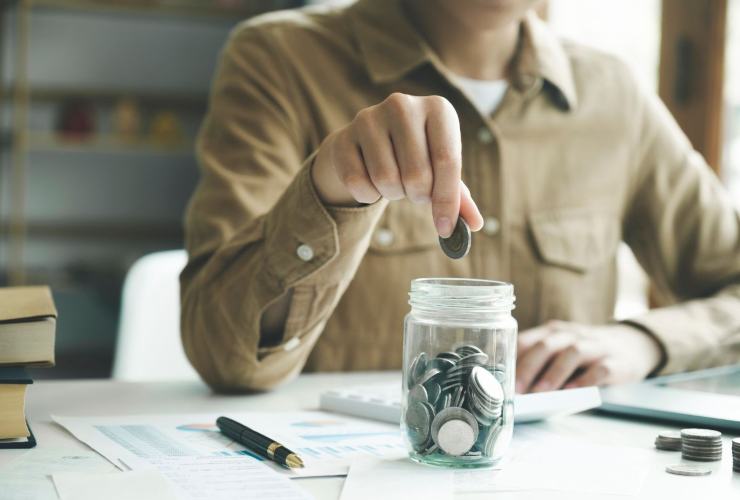 persona che mette una moneta in un vasetto di vetro
