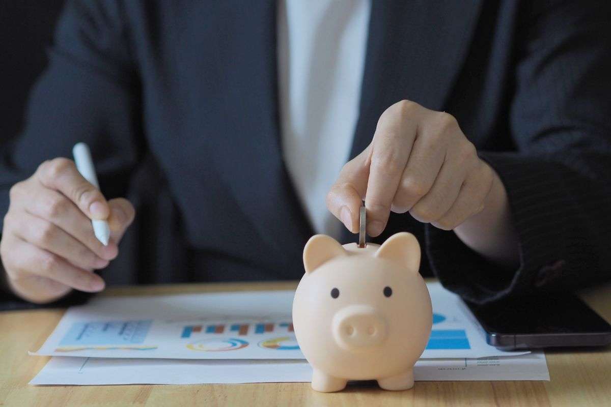 Persona che fa calcoli e mette moneta in un salvadanaio
